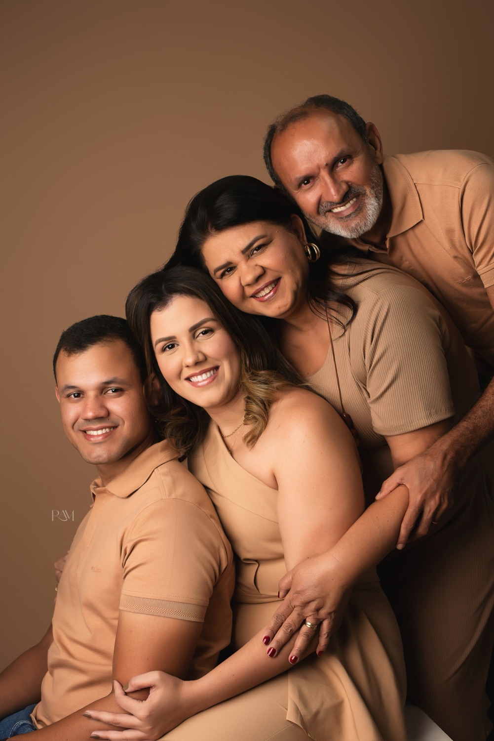 Três gerações de uma família abraçadas em fundo marrom